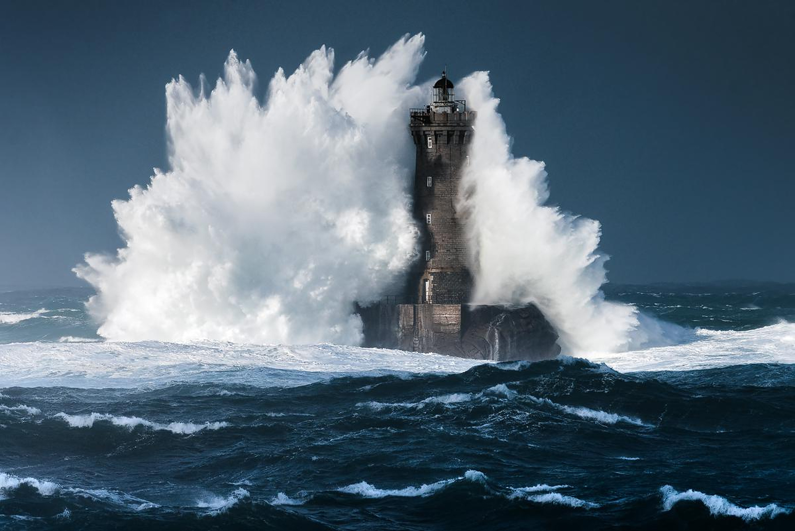 A lighthouse standing firm as a storm wave breaks over it